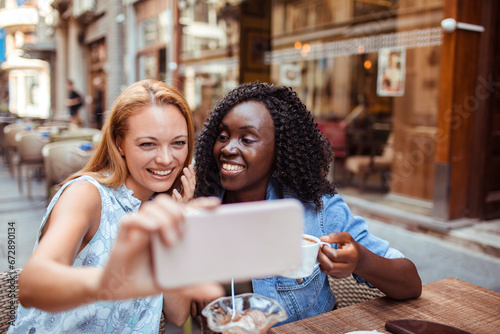 Two happy girlfriends holding smartphone in outdoor cafe