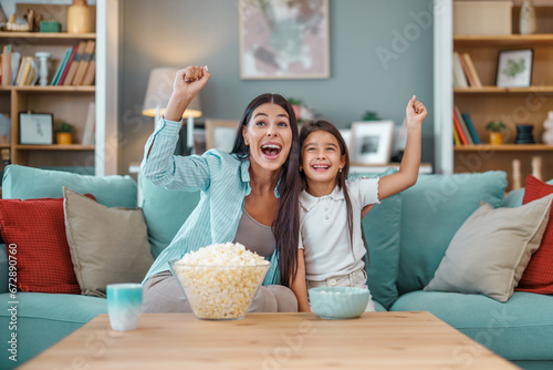 Happy young mom and her daughter watching football game on television photo