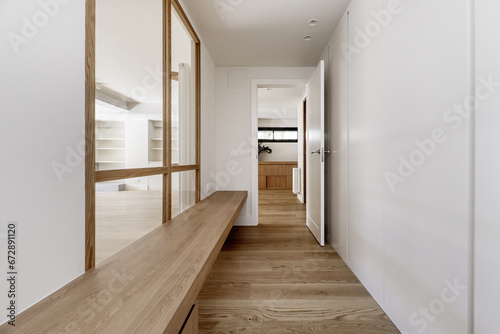 Hallway of a home with white wooden built-in wardrobes, a long wooden bench next to a skylight with a wooden structure and integrated white ceiling spotlights