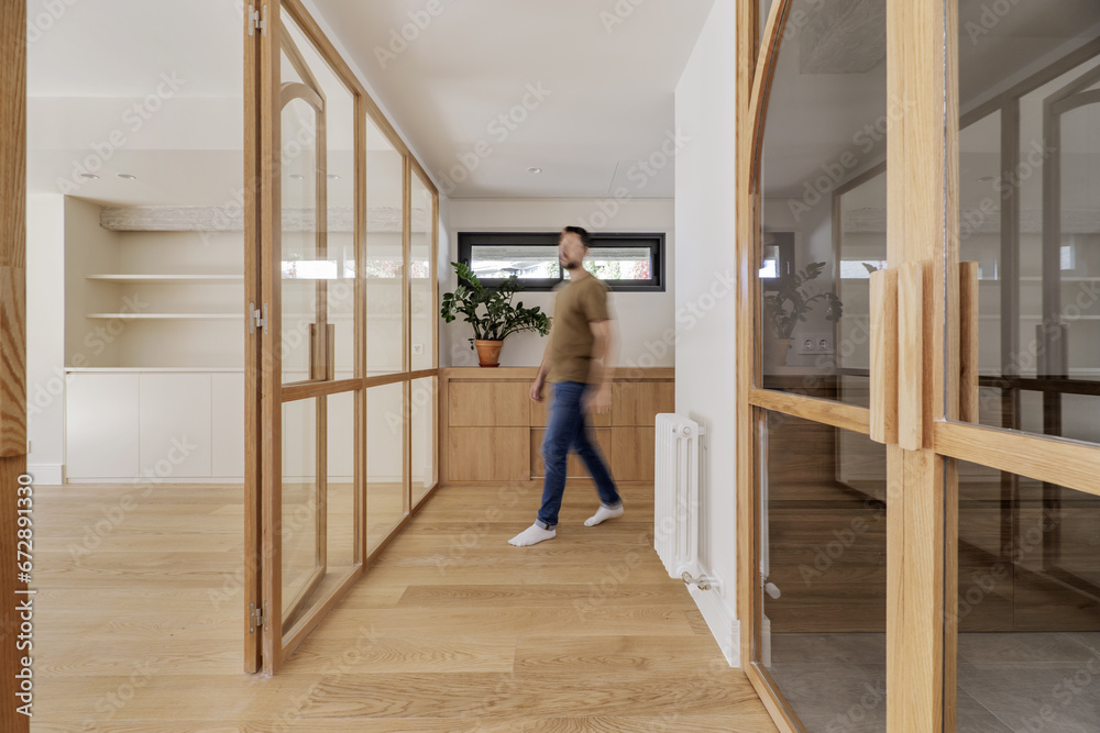 A man entering the hallway of a home with access to a living room with a glass and wood wall A man entering the hallway of a home with access to a living room with a glass and wood wall