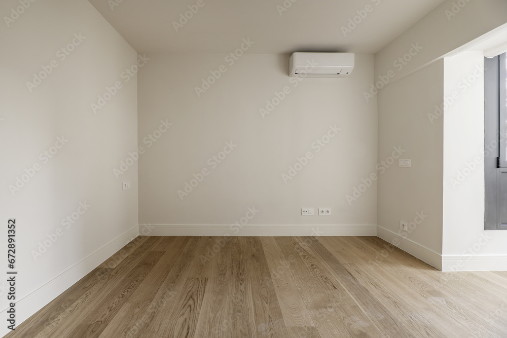 Obraz premium Empty room with plain off-white painted walls, wooden floors and an air conditioner on one wall