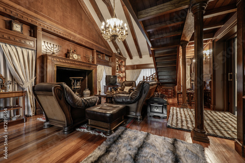 Billede på lærred Room decorated with a lot of noble wood in the furniture and on the walls, a staircase to the library of the same material and a wooden sofa upholstered in brown cowhide