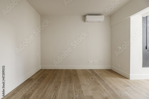 Empty room with plain off-white painted walls  wooden floors and an air conditioner on one wall
