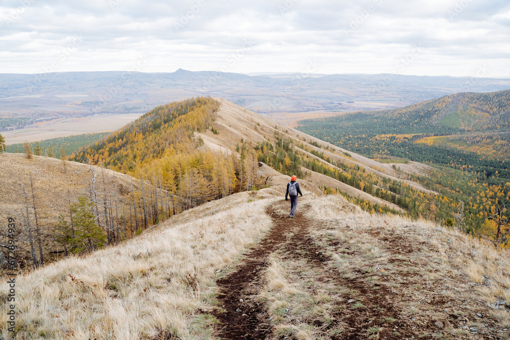 Beautiful autumn landscape, man descending from the mountain, rear view, black path walking on top of the hill, trekking in the mountains, nature vacation.