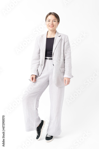 Young caucasian woman, professional entrepreneur standing in office clothing, smiling and looking confident on white background. Full length portrait