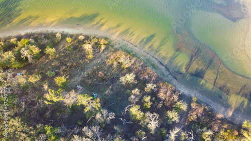 Curved shoreline and remote waterfront primitive camping sites with tents at Isle du Bois Ray Roberts Lake State Park lush green tree forest near Denton, Texas, US aerial view