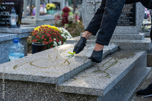 Preparing a grave for All Saints' Day celebrated on November 1st, a woman cleans and washes a marble tomb using a special cleaning solution, brush, cloth, and water. The tomb is clean.