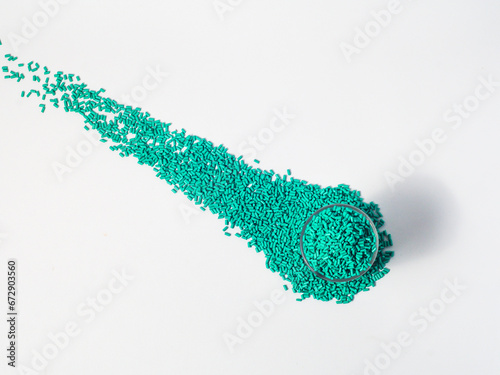 Turquoise masterbatch granules of cold cut type, placed in a glass cup on a white background, this material is used as a colorant for products in the plastics industry