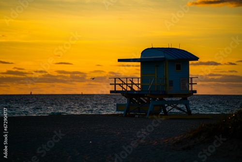 Beach lifeguard tower in the foreground, illuminated by the golden light of a stunning sunset. © Wirestock