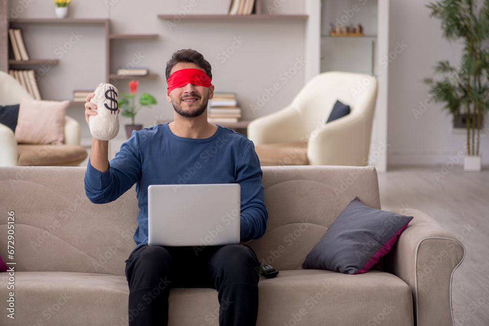 Young blindfolded man holding moneybag at home