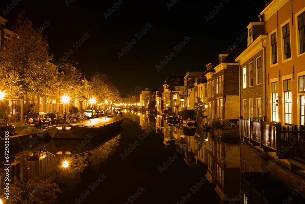 Fleet of boats in a canal in front of a picturesque row of houses at night: Leiden