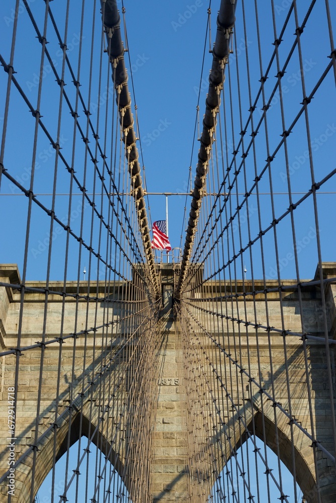 Fototapeta premium American flag waving atop the iconic Brooklyn Bridge located in New York City