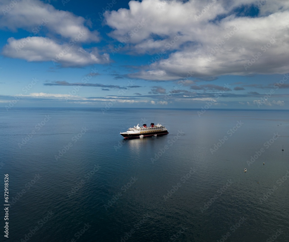 Aerial view of a ship sailing in a sea under a cloudy blue sky