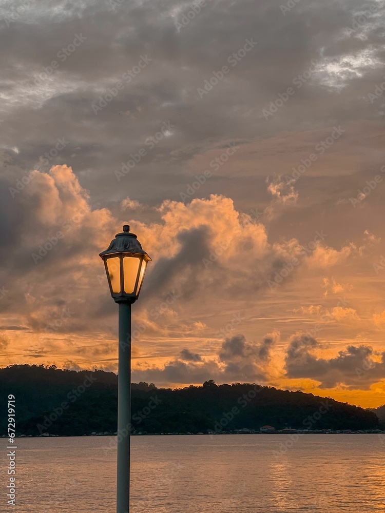 Lit street lamp on the background of a sunset in the cloudy sky over the shore Lit street lamp on the background of a sunset in the cloudy sky over the shore