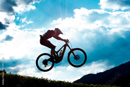 Fototapeta Naklejka Na Ścianę i Meble -  Mountain Bike Downhill Fahrer im Gegenlicht bei Sprung während Wettkampf – MTB Rider Jumping Silhouette