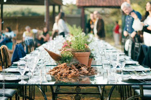 Outdoor dining setup for a sophisticated event featuring crystal glassware, polished plates, and a rustic wooden centerpiece surrounded by fresh potted herbs