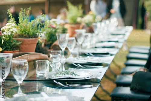 Outdoor dining setup for a sophisticated event featuring crystal glassware, polished plates, and a rustic wooden centerpiece surrounded by fresh potted herbs