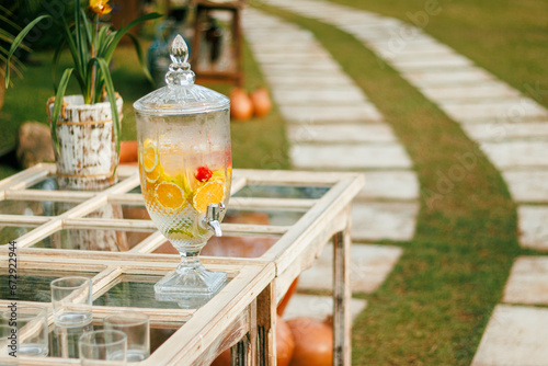 Crystal beverage dispenser filled with citrus-infused water on a rustic outdoor table, casting a warm glow in a garden setting