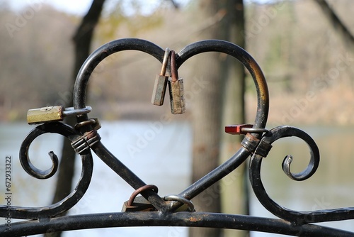 Close-up shot of two padlocks of different sizes that are securing a metal heart-shaped gate