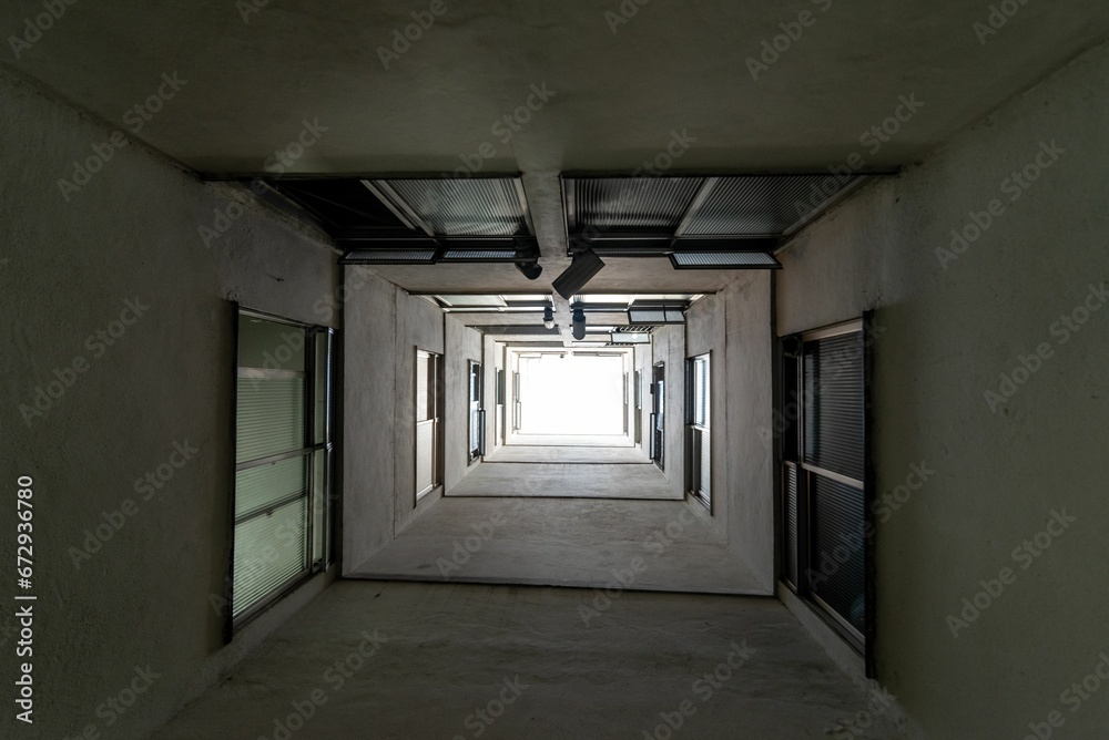 Long, cement corridor with multiple doors, windows running along the length of the hallway