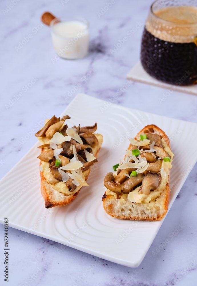 Sandwiches on a baguette with hummus, oyster mushrooms and parmesan cheese on a white ceramic plate on a marble background. Modern style in food photography, minimalism. Sandwiches on a baguette with hummus, oyster mushrooms and parmesan cheese on a white ceramic plate on a marble background. Modern style in food photography, minimalism.