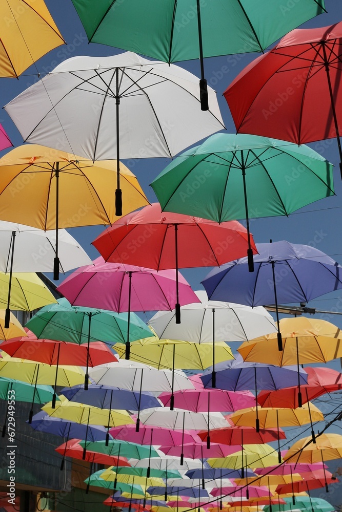 Obraz premium Low angle shot of colorful umbrellas hanging on wire in a narrow city alley