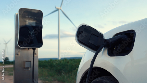 Progressive future energy infrastructure concept of electric vehicle being charged at charging station powered by green and renewable energy from a wind turbine in order to preserve the environment.