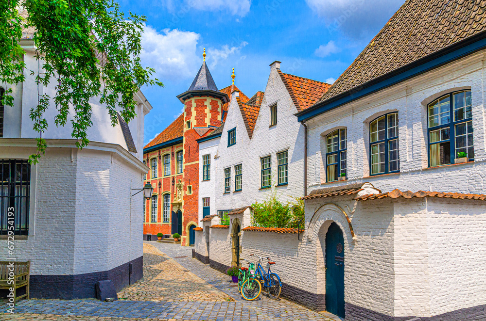 Beguinage Courtrai of Saint-Elisabeth, Begijnhof van Kortrijk with white houses and Sint-Annazaal museum, bicycles near wall on narrow cobblestone street in Kortrijk city historical centre, Belgium - obrazy, fototapety, plakaty 