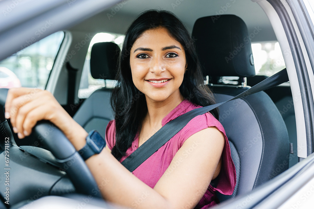 Portrait of young indian woman smiling at camera sitting on driver's seat in car