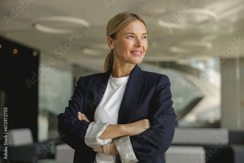 Photos Portrait of smiling female entrepreneur with crossed hands standing in office an