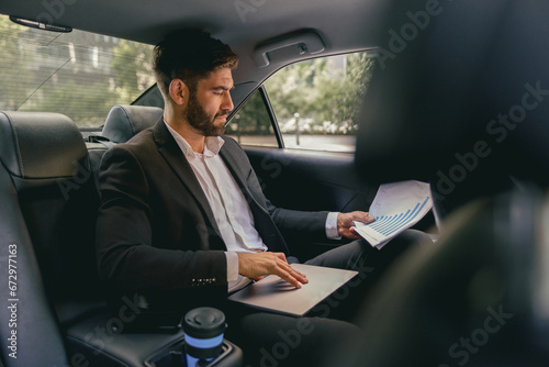 Confidence businessman sitting on car backseat and working with documents and use laptop © Yaroslav Astakhov