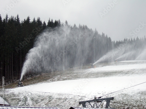 A snow cannon produces a cloud of snow on a mountain hill of a ski resort