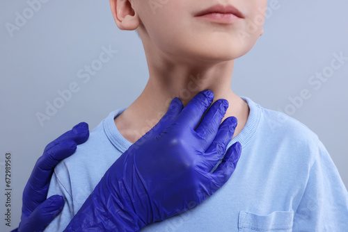 Endocrinologist examining boy s thyroid gland on light grey background  closeup