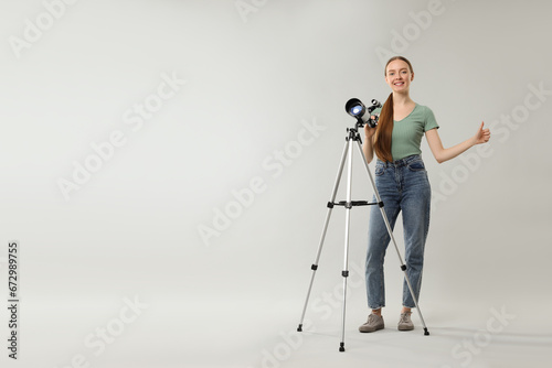 Happy astronomer with telescope showing thumbs up on grey background, space for text
