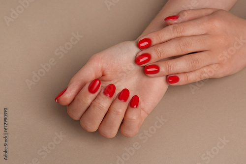 Woman with red polish on nails on beige background, closeup