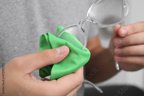 Man wiping glasses with microfiber cloth indoors  closeup