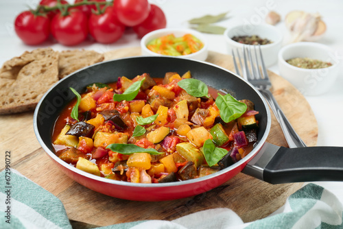 Frying pan with tasty ratatouille on wooden board