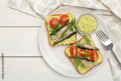 Delicious sandwiches with sprats, tomatoes, dill and avocado puree served on white wooden table, top view. Space for text