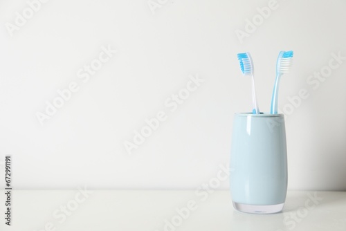 Plastic toothbrushes in holder on white table  space for text