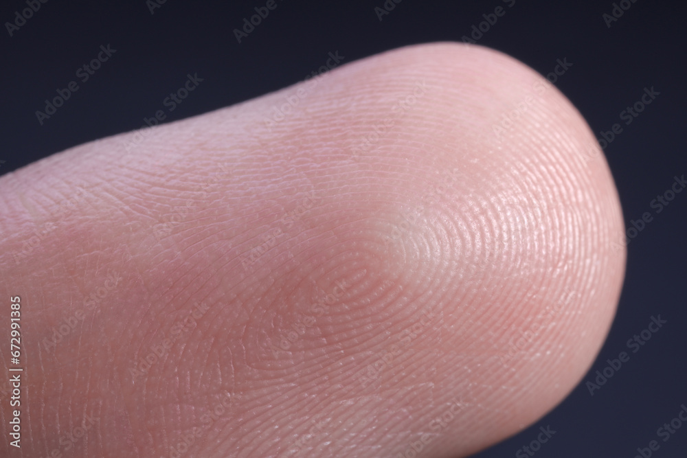 Finger with friction ridges on dark background, macro view Finger with friction ridges on dark background, macro view