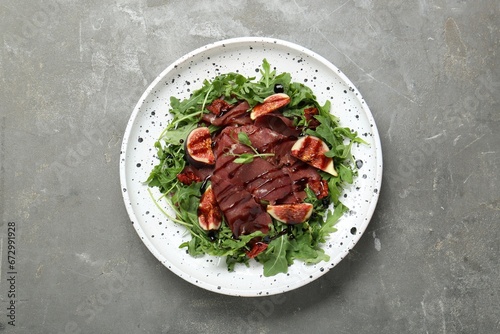 Plate of tasty bresaola salad with figs, sun-dried tomatoes and balsamic vinegar on grey table, top view