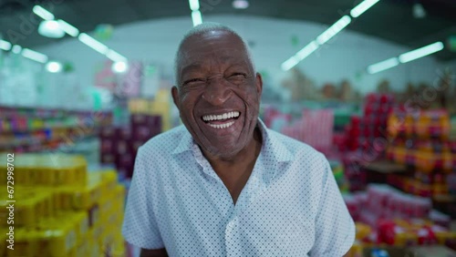 One happy black Brazilian senior man smiling and laughing standing inside grocery shed with consumer products in background photo
