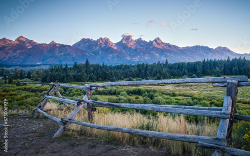 Rustic fence extends below the Grand Tetons at sunrise photo