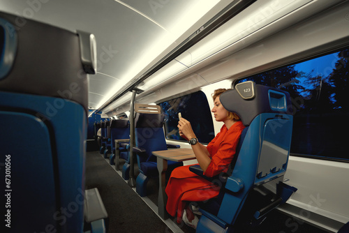 Public transport with woman in train on commute into city or work during evening time. Train travel and reading on mobile phone social media,  notifications, messages  or video. Copy space.