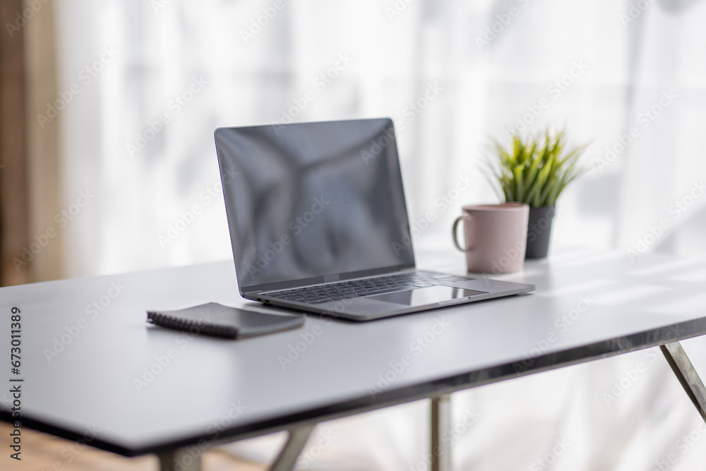 Laptop Computer, notebook, and eyeglasses sitting on a desk in a large open plan office space after working hours	