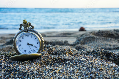 a gold pocket watch sits on a sandy beach, accompanied by the soothing waves of the beach