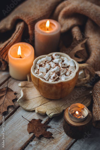 Spicy sweet fall hot drink: delicious pumpkin latte with cinnamon, marshmallow with salted caramel. Served in handmade artisan mug in shape of pumpkins, cozy home decor with candles, dry autumn leaves