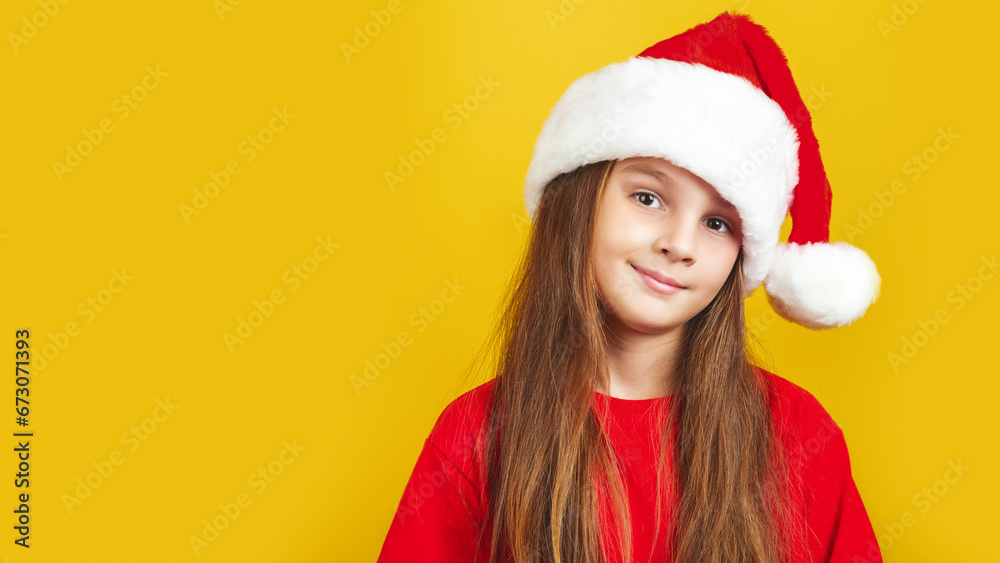 Сute little girl wearing Christmas Santa hat standing isolated over yellow background, looking at camera
