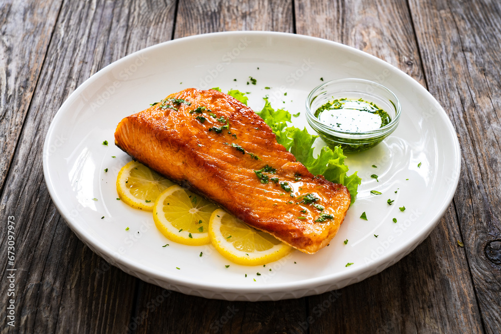 Seared salmon steak with lettuce and lemon on wooden table
