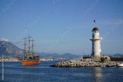 Wallpaper Mural Lighthouse at the harbor of the Turkish city of Alanya, Antalya region, Turkey. A pirate ship for tourists, recreated from historical times, is just passing the harbor entrance. Torontodigital.ca